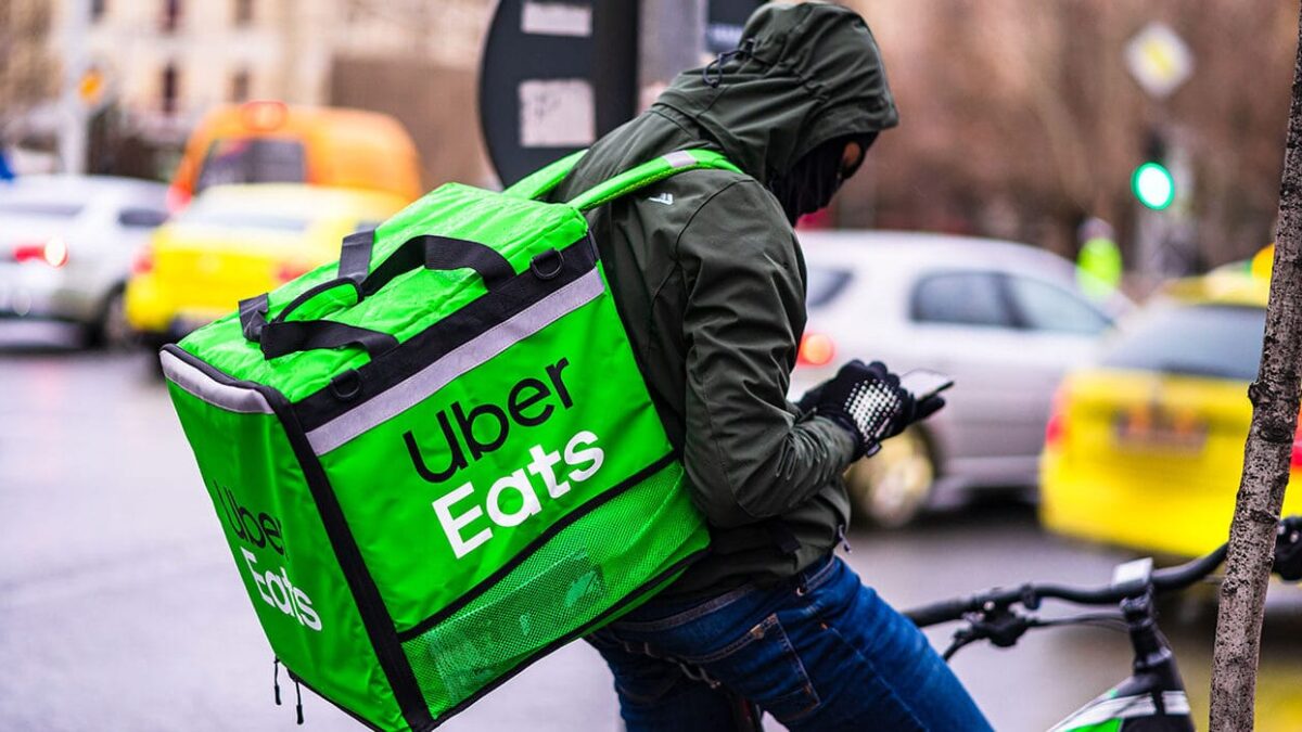 Young man on a bike with Uber Eats logo delivering food during a rainy day in Bucharest, Romania,
