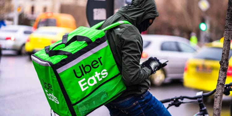 Young man on a bike with Uber Eats logo delivering food during a rainy day in Bucharest, Romania,